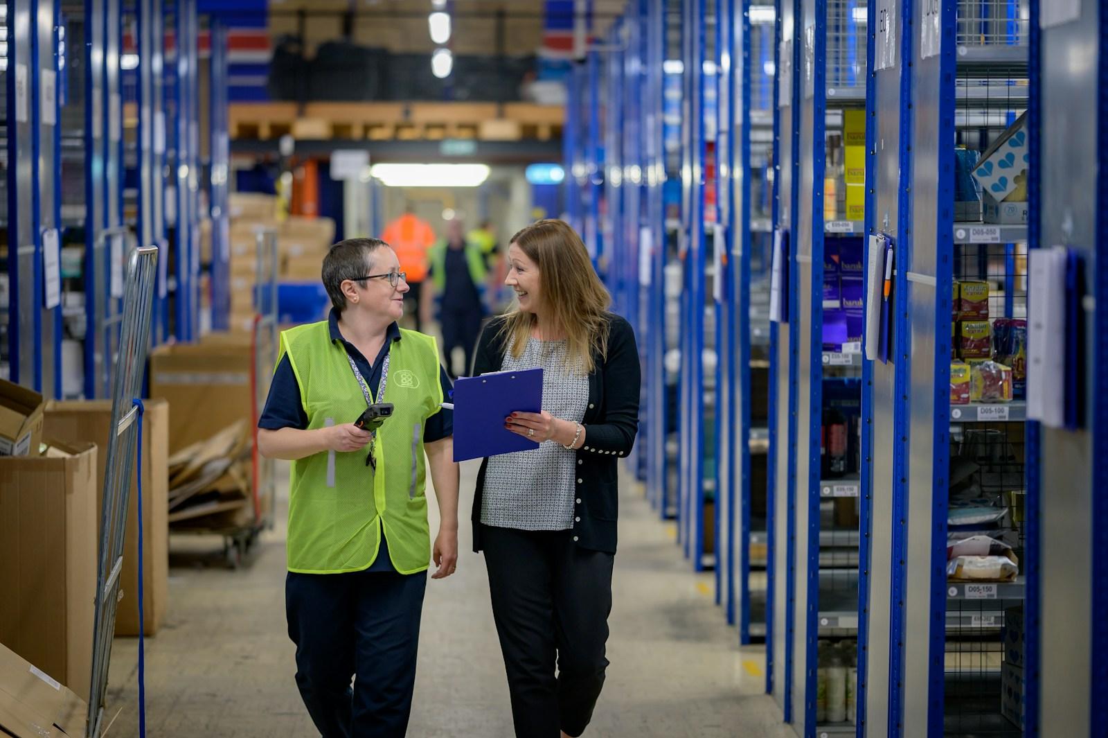 Two colleagues walking a warehouse aisle with a clipboard