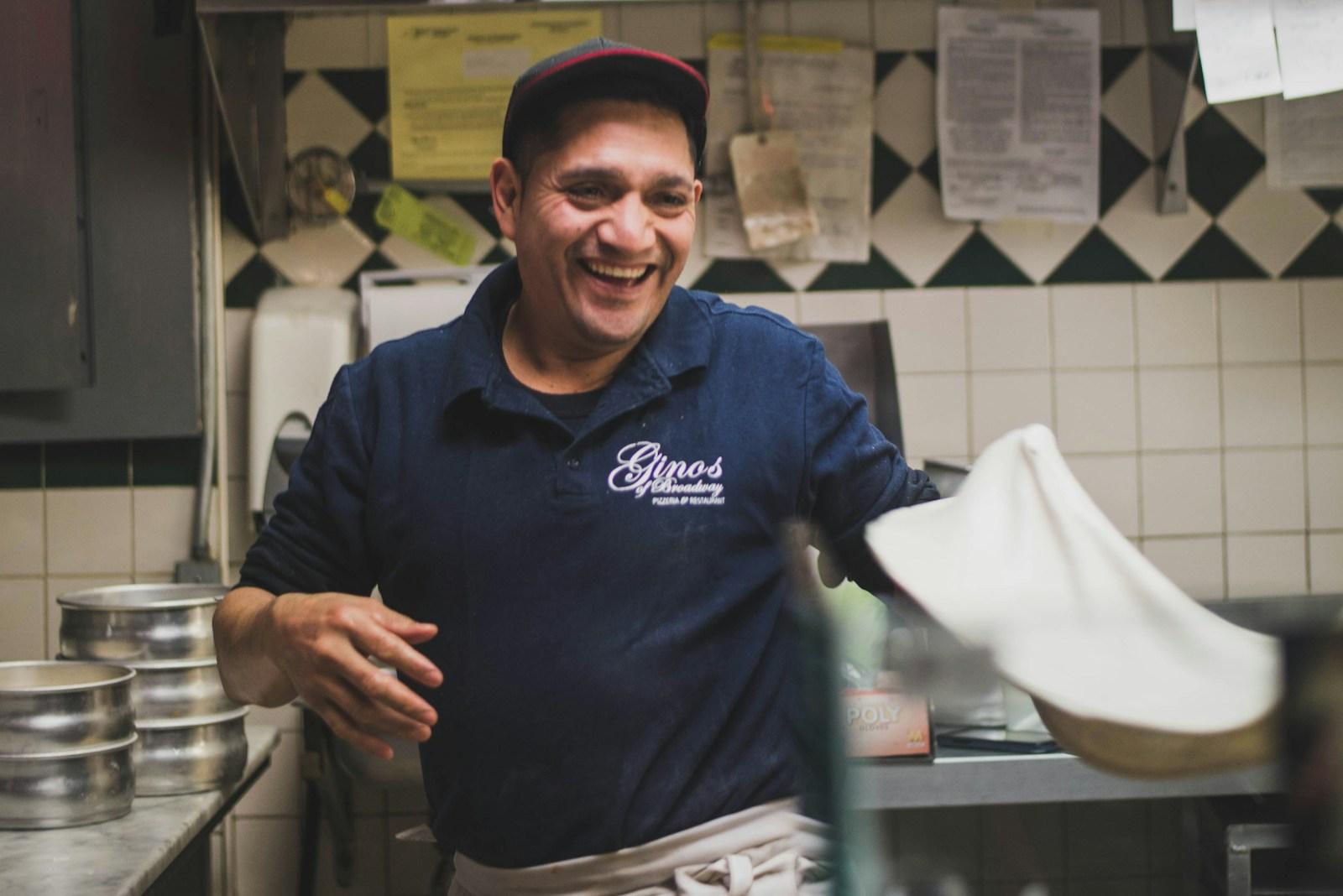 A smiling restaurateur stretching pizza dough in his kitchen