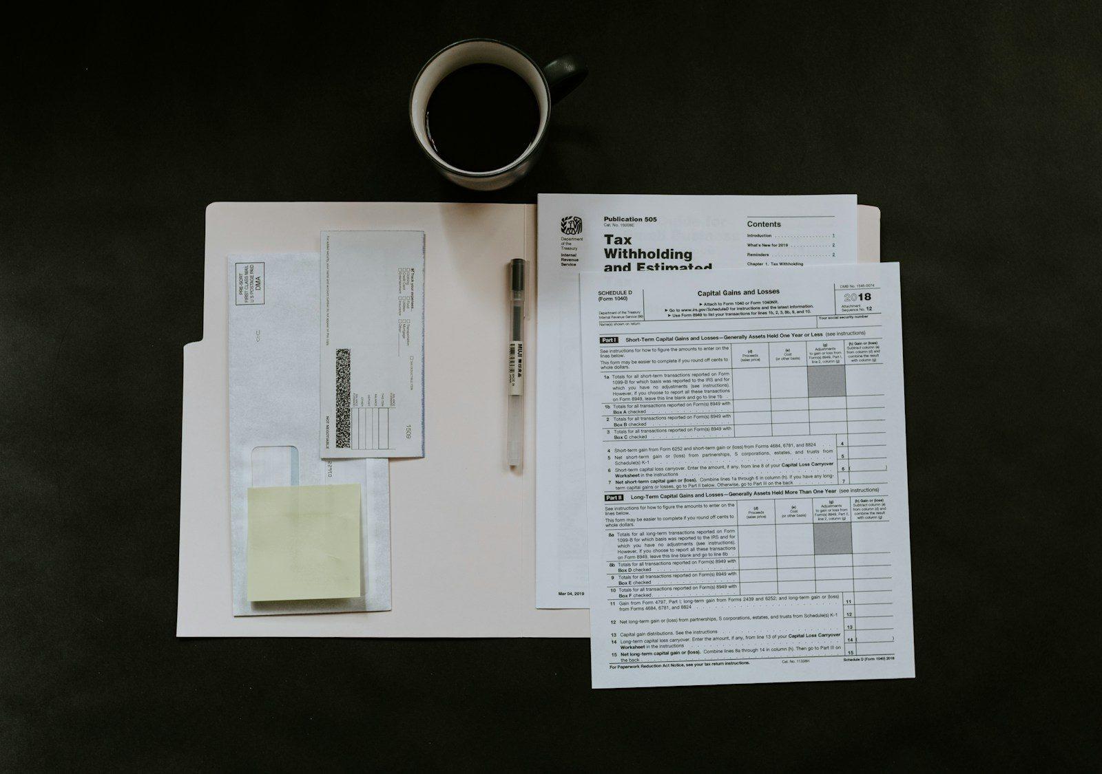 Tax forms, a pen and a coffee mug on a desk.