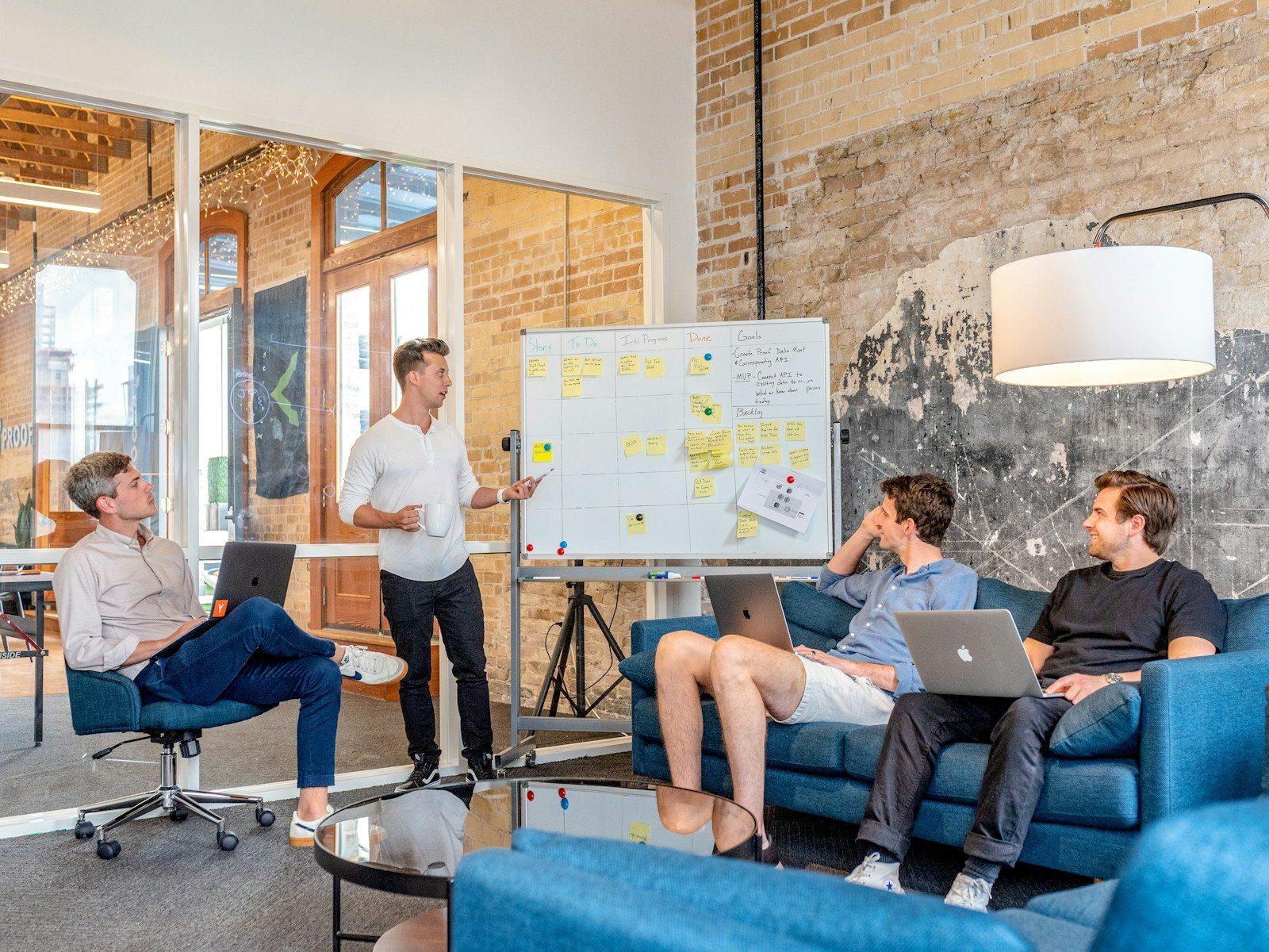 A small team in a loft office, one person presenting at a whiteboard.